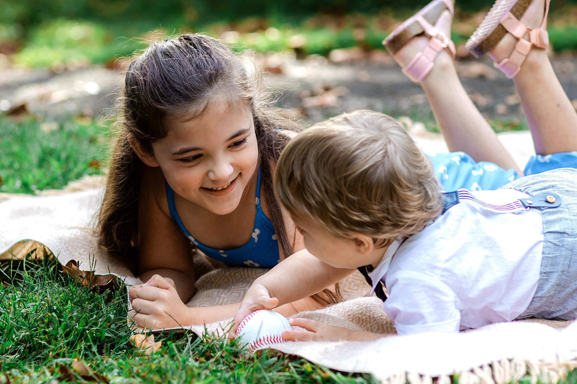 Brother and sister holding a baseball laying on a blanket