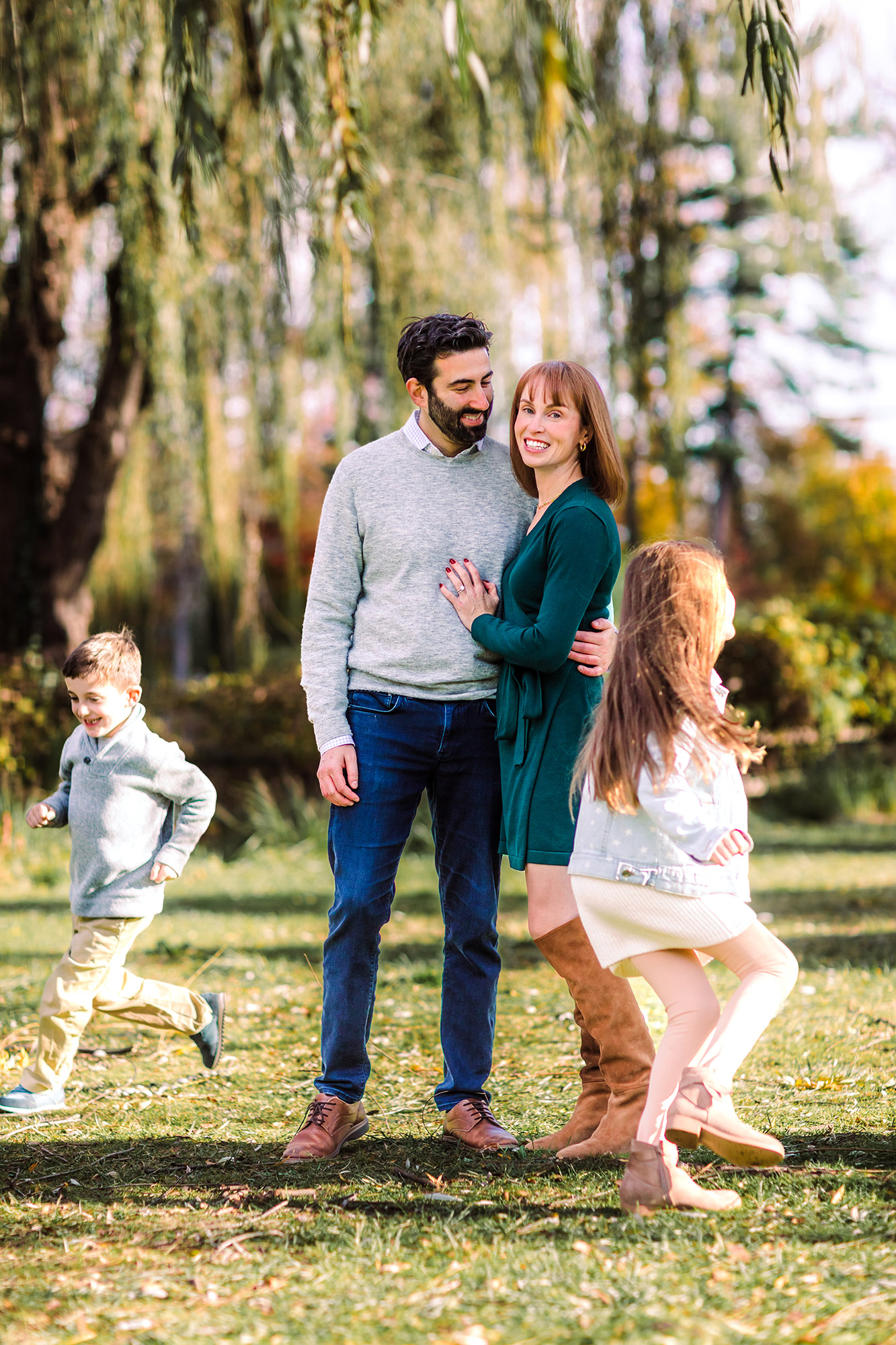 Two young kids running around their parents in a park