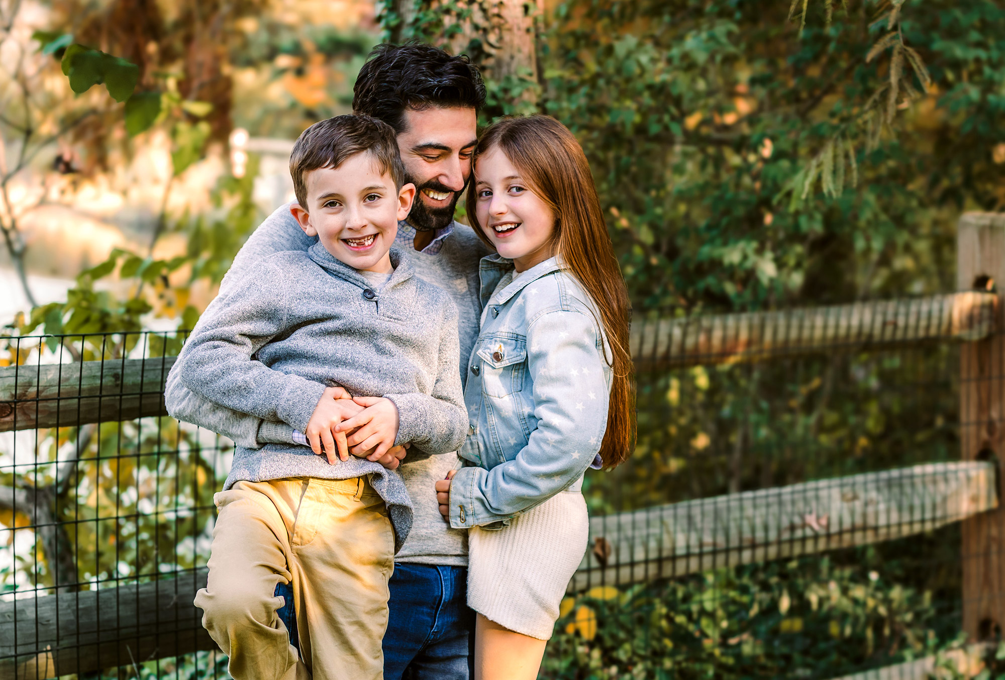 a dad with his two kids photographed against a fence