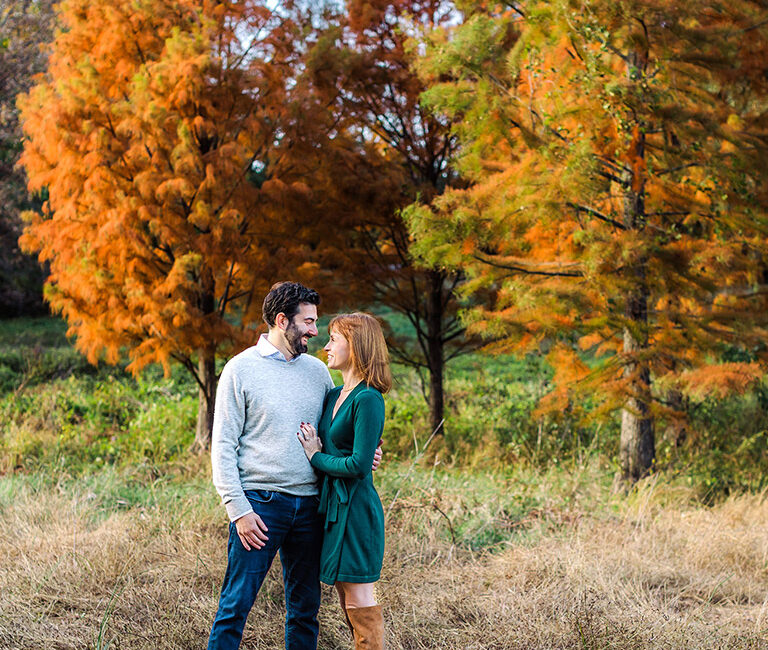 Couple standing in a field surrounded by colorful fall trees