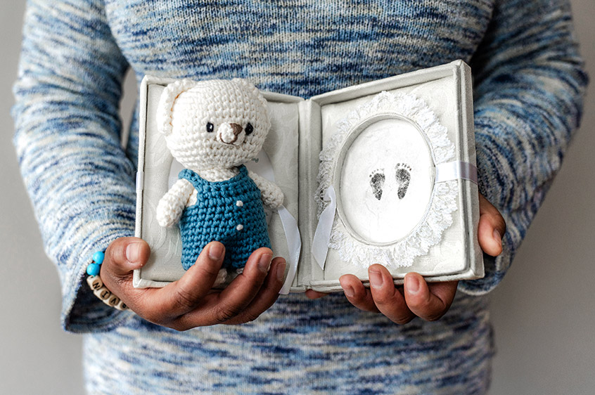 closeup of mother holding pregnancy loss footprints and bear