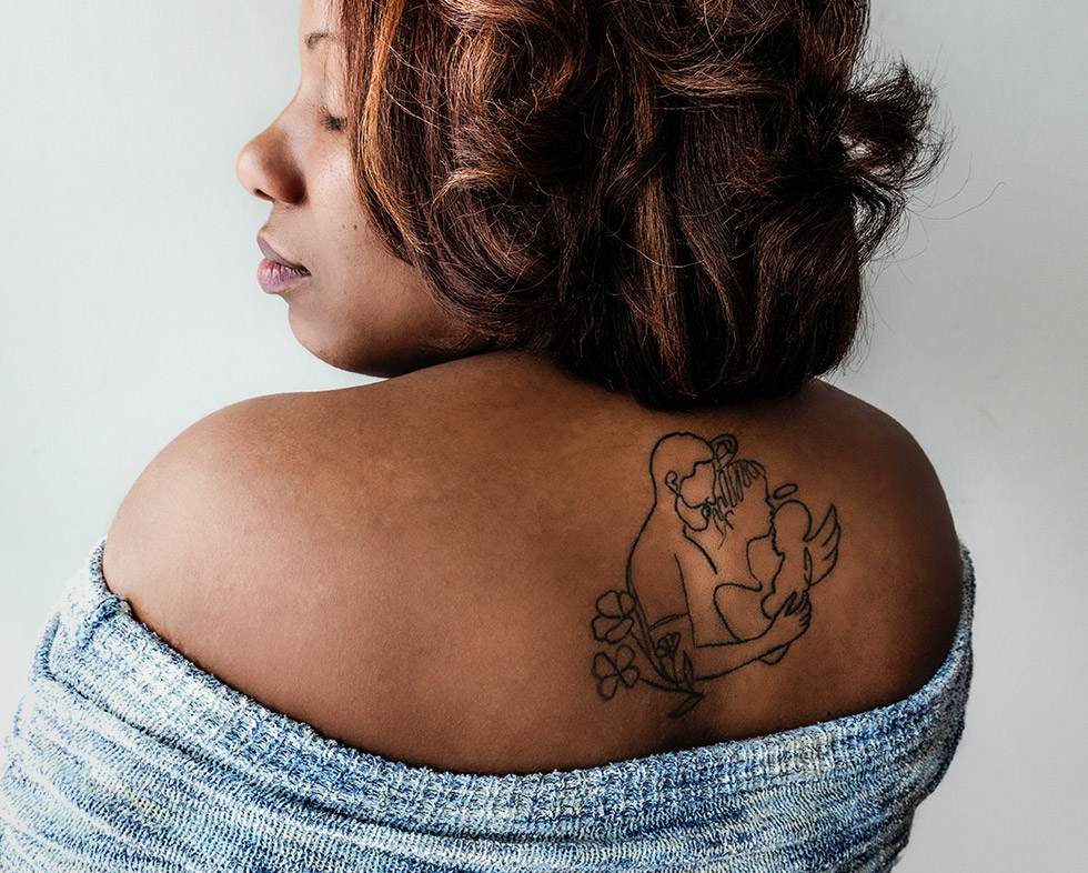 a portrait of a woman with a tattoo depicting a mother and father holding an angel baby