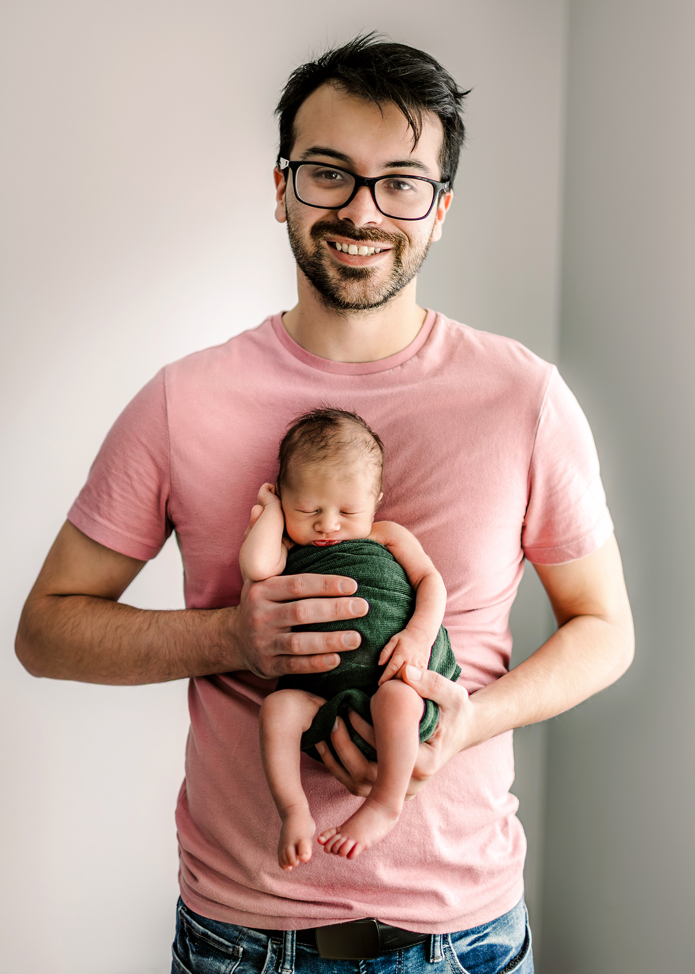 Dad in pink holding his newborn in green swaddle