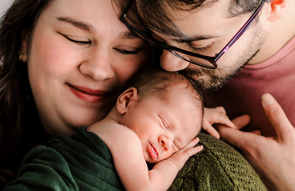 Mom holding her newborn on her shoulder while dad kisses the head