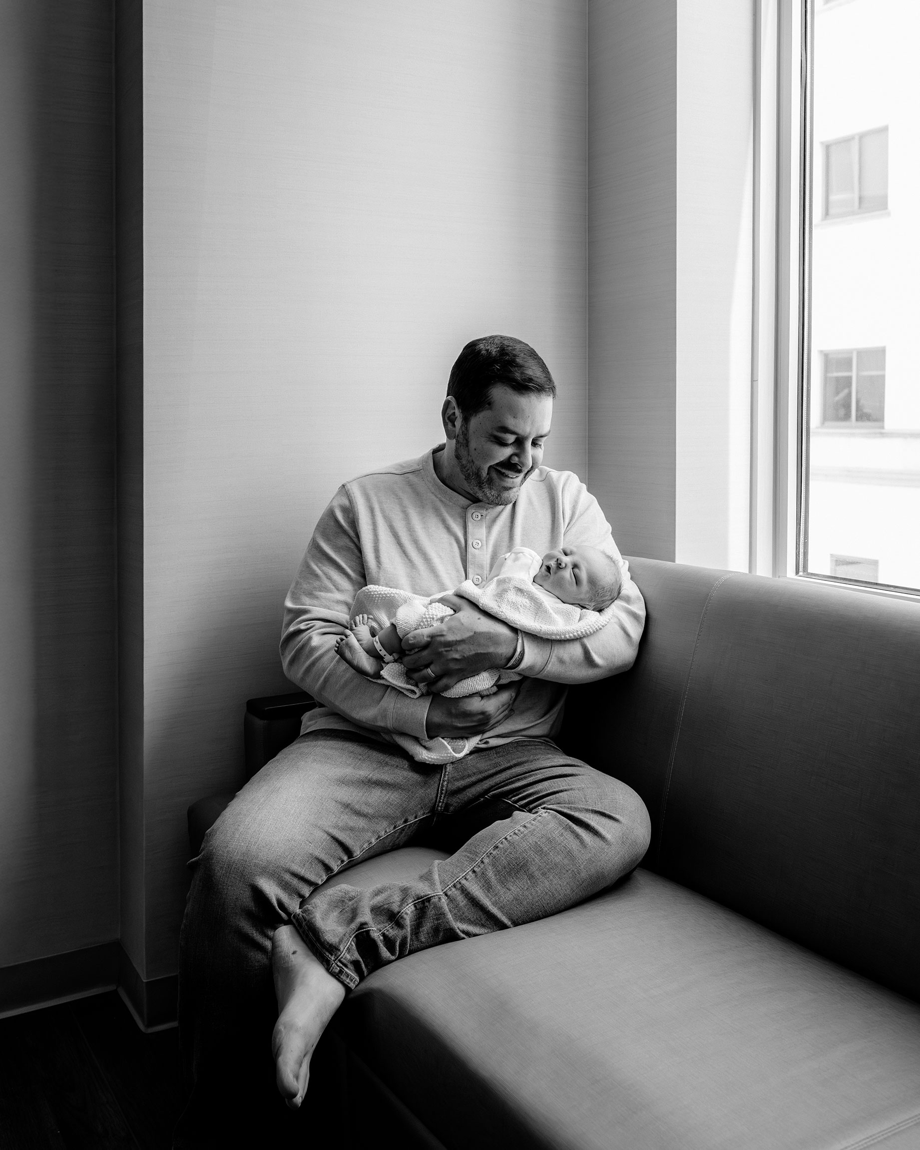dad holding newborn while sitting on the hospital couch