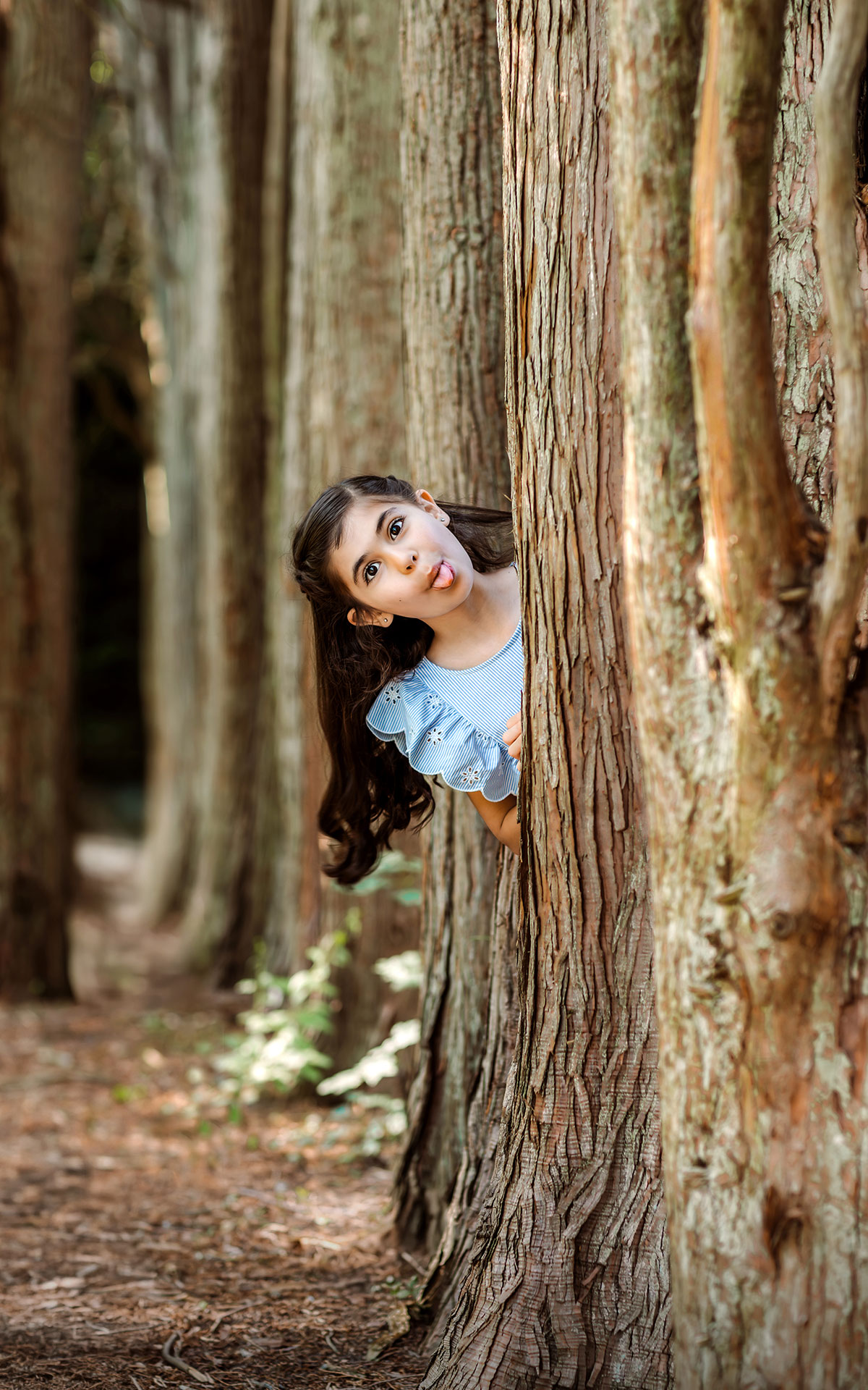 Little girl peeking out from between trees and sticking out her tongue